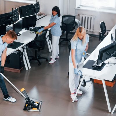 Cleans floor. Group of workers clean modern office together at daytime Cleans floor. Group of workers clean modern office together at daytime.