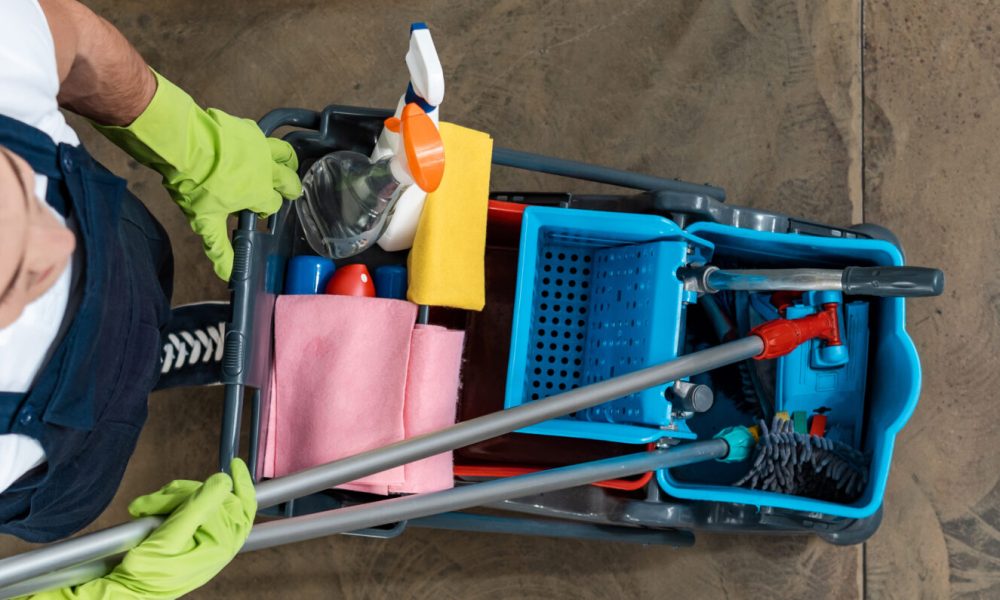 top view of cleaner in uniform carrying cart with cleaning supplies, panoramic shot top view of cleaner in uniform carrying cart with cleaning supplies, panoramic shot